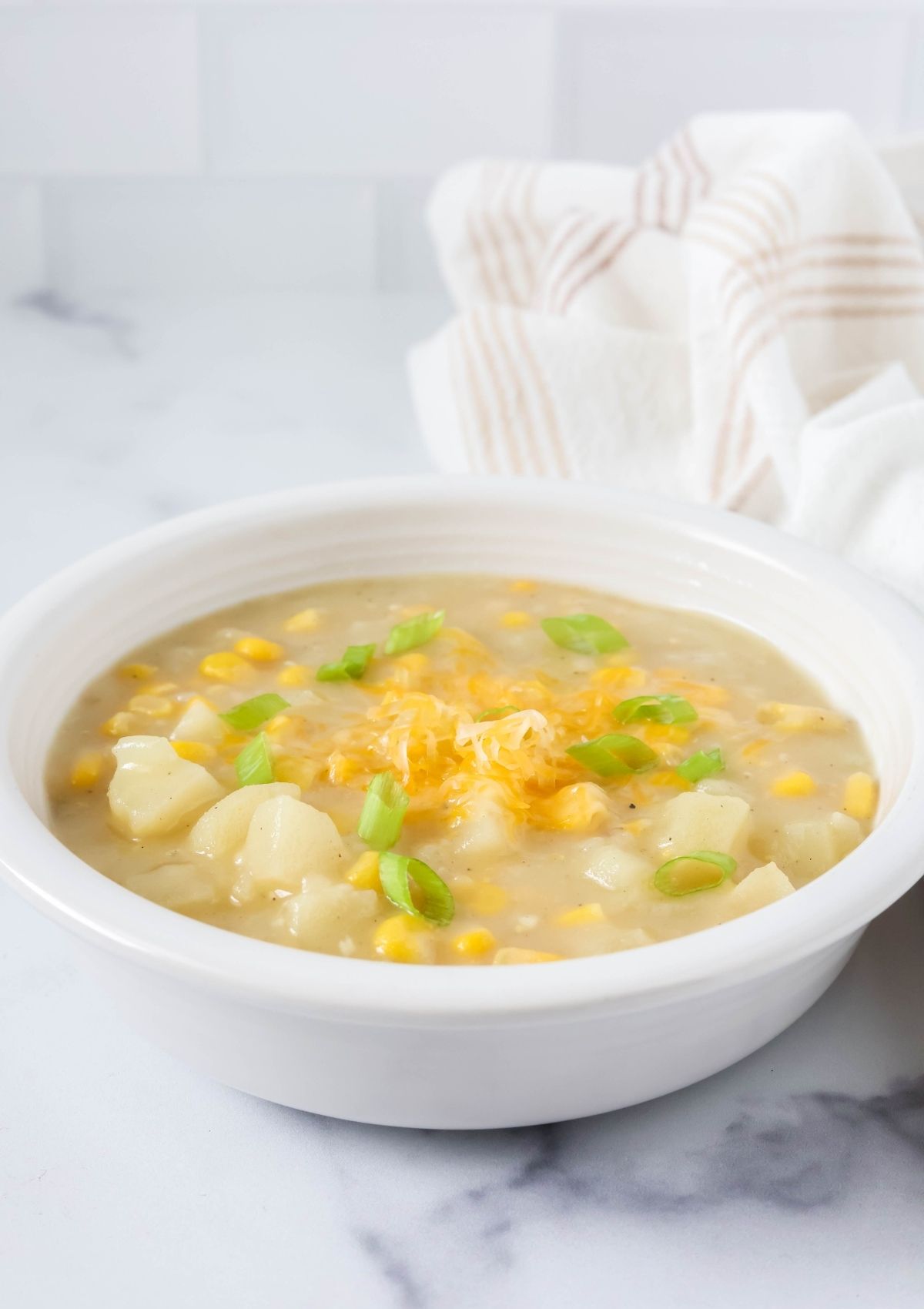 A white bowl filled with creamy potato corn soup made with canned corn and frozen hash brown potatoes. The soup is garnished with cheese and green onions.