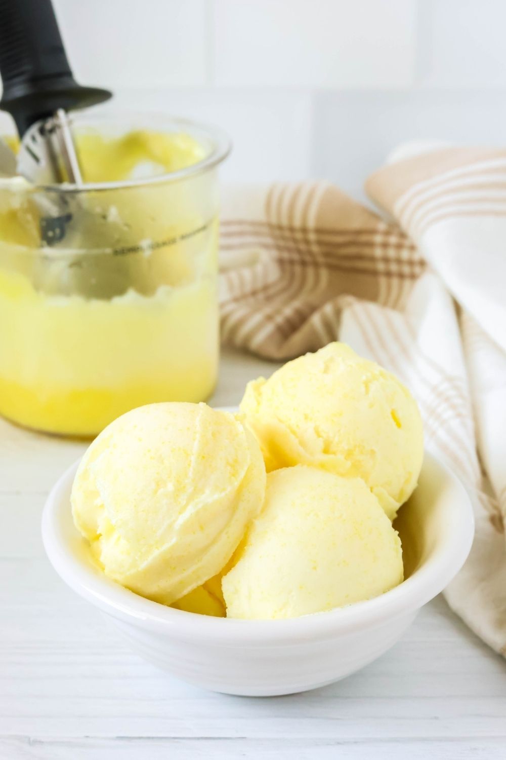 White bowl of dairy free lemon sorbet made in the Ninja Creami machine. In the background is a pint of remaining sorbet.