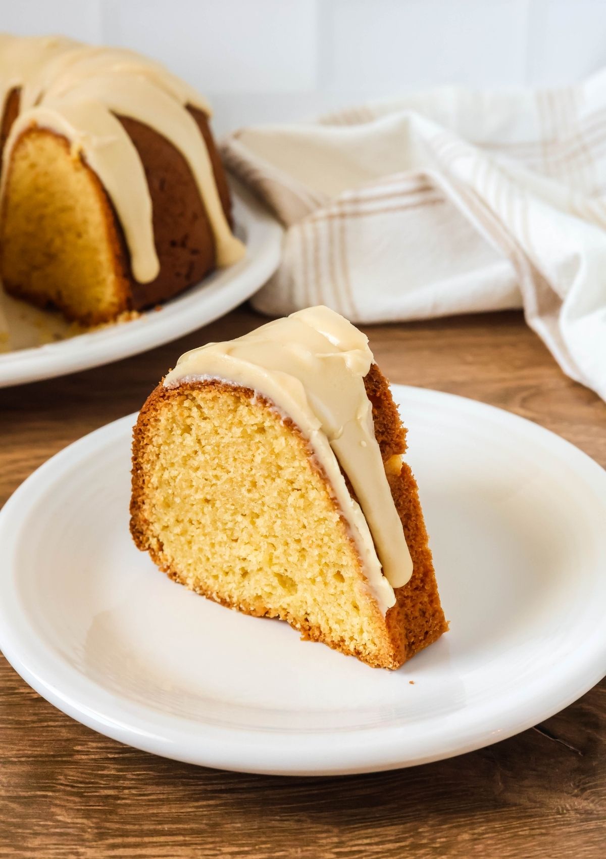 Slice of easy glazed brown sugar pound cake on a white plate. The remainder of the bundt cake is in the background.