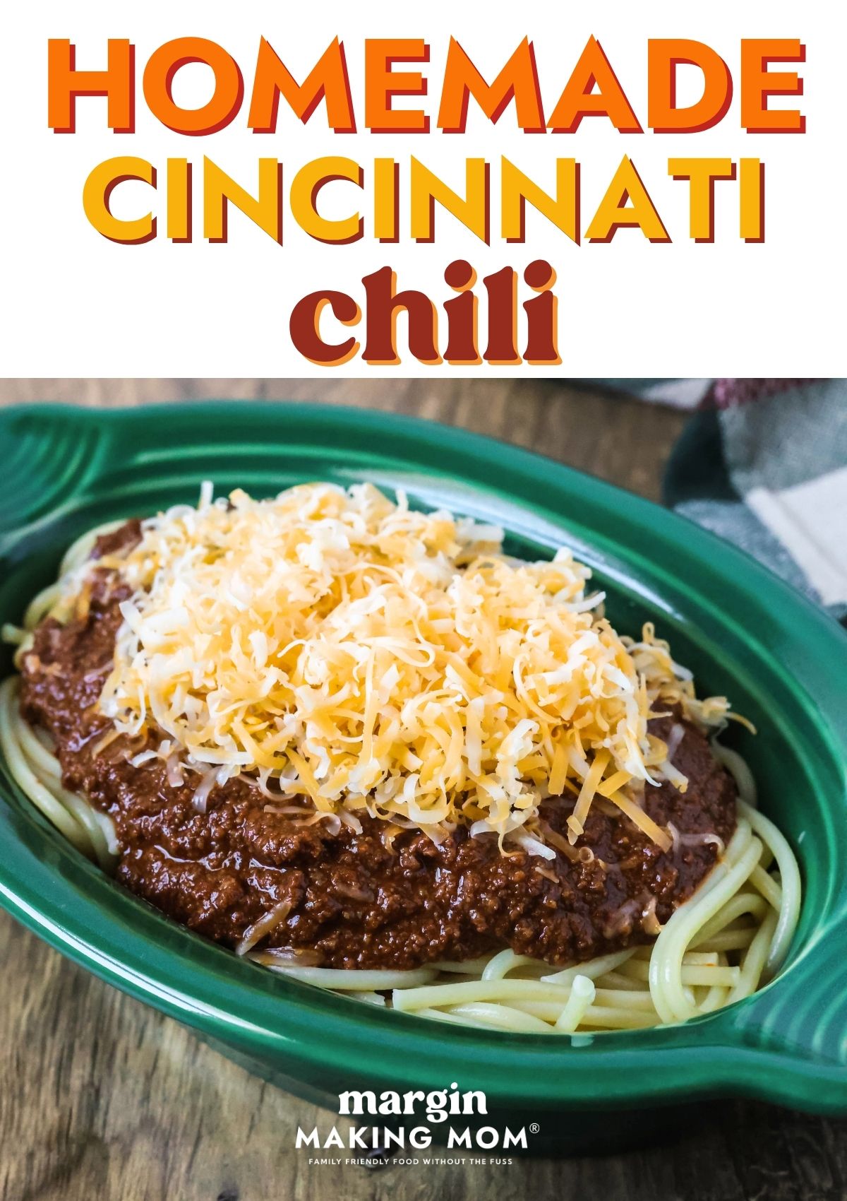 Homemade Cincinnati chili served over spaghetti in a green dish and topped with shredded cheese.