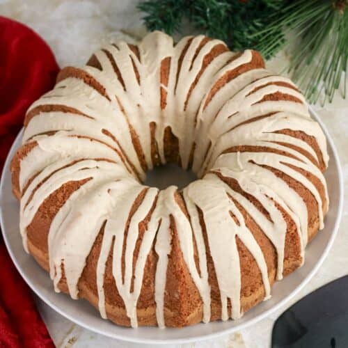 Eggnog pound cake topped with eggnog glaze is served on a white cake plate.