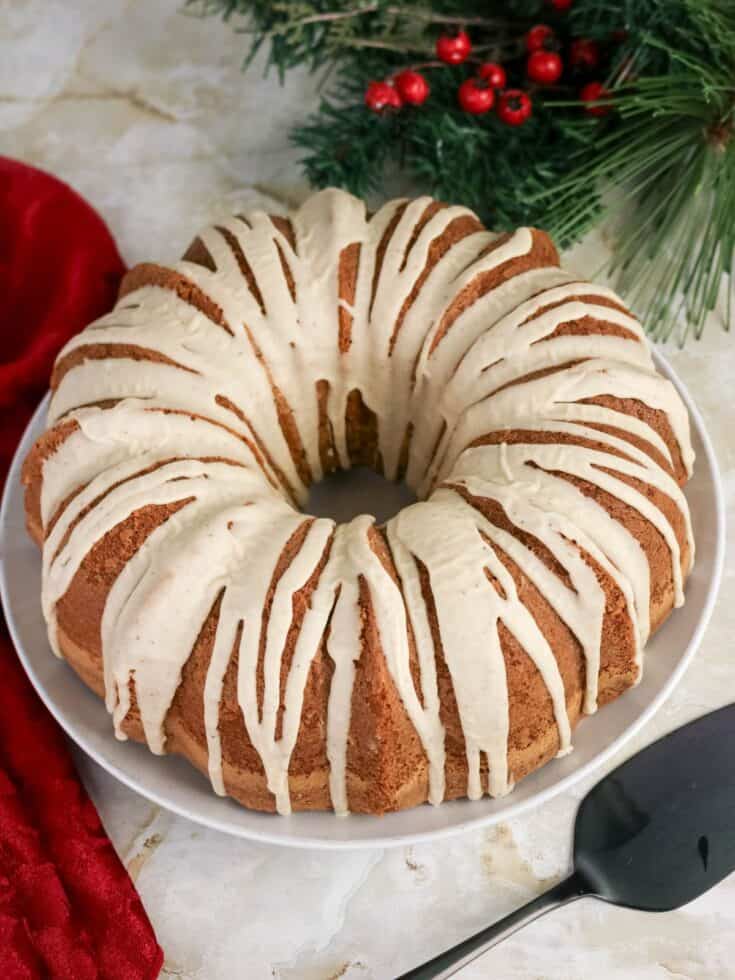 Eggnog pound cake topped with eggnog glaze is served on a white cake plate.