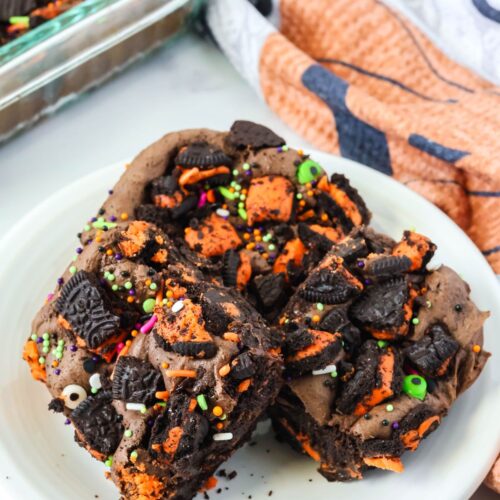 Halloween Oreo cake bars served on a white plate. The baking dish of remaining bars is in the background.