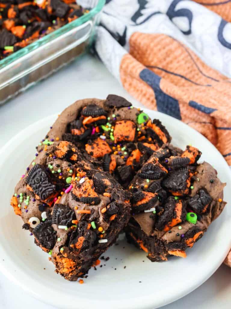 Halloween Oreo cake bars served on a white plate. The baking dish of remaining bars is in the background.