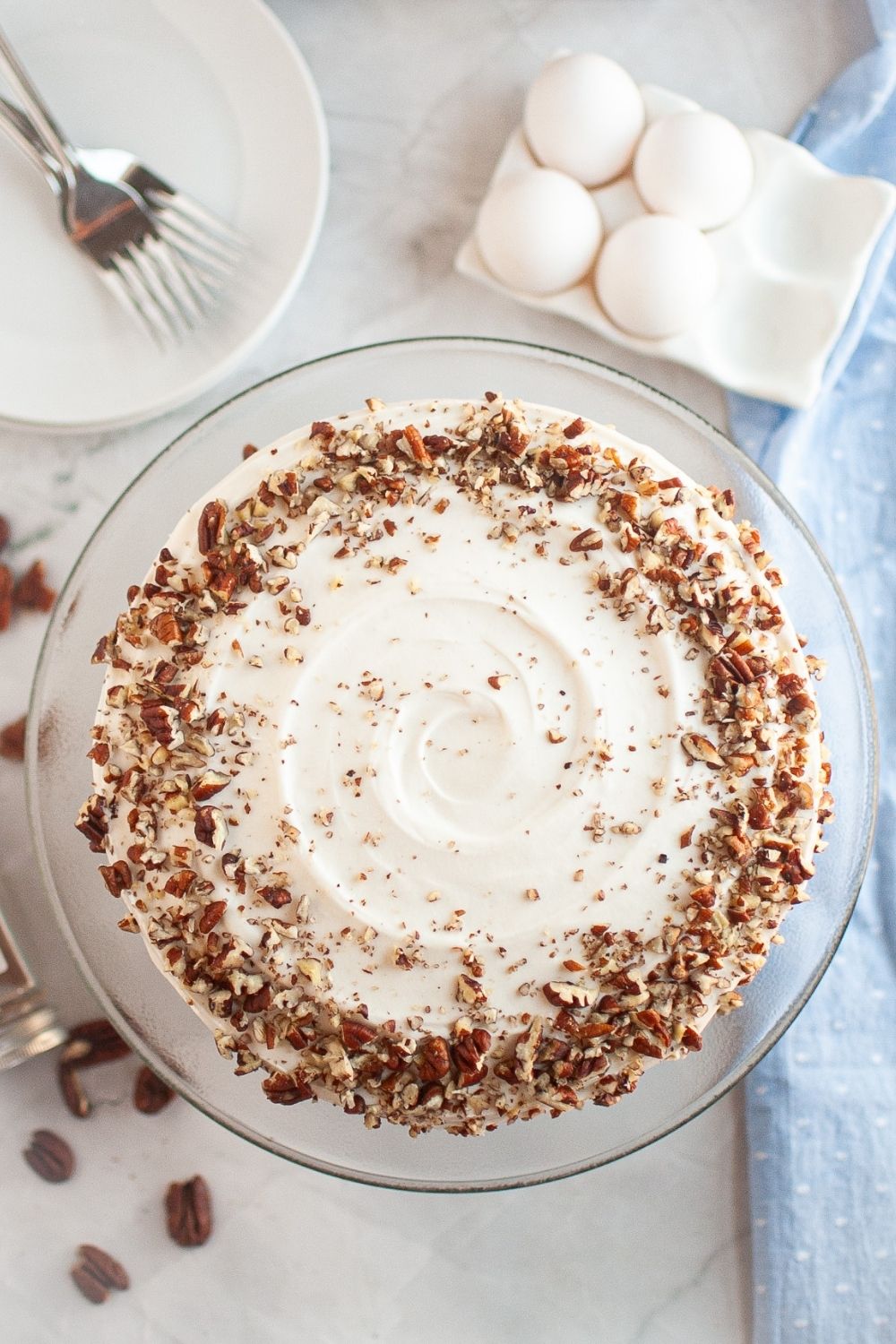 Overhead view of a homemade carrot cake topped with cream cheese frosting and garnished with chopped pecans.