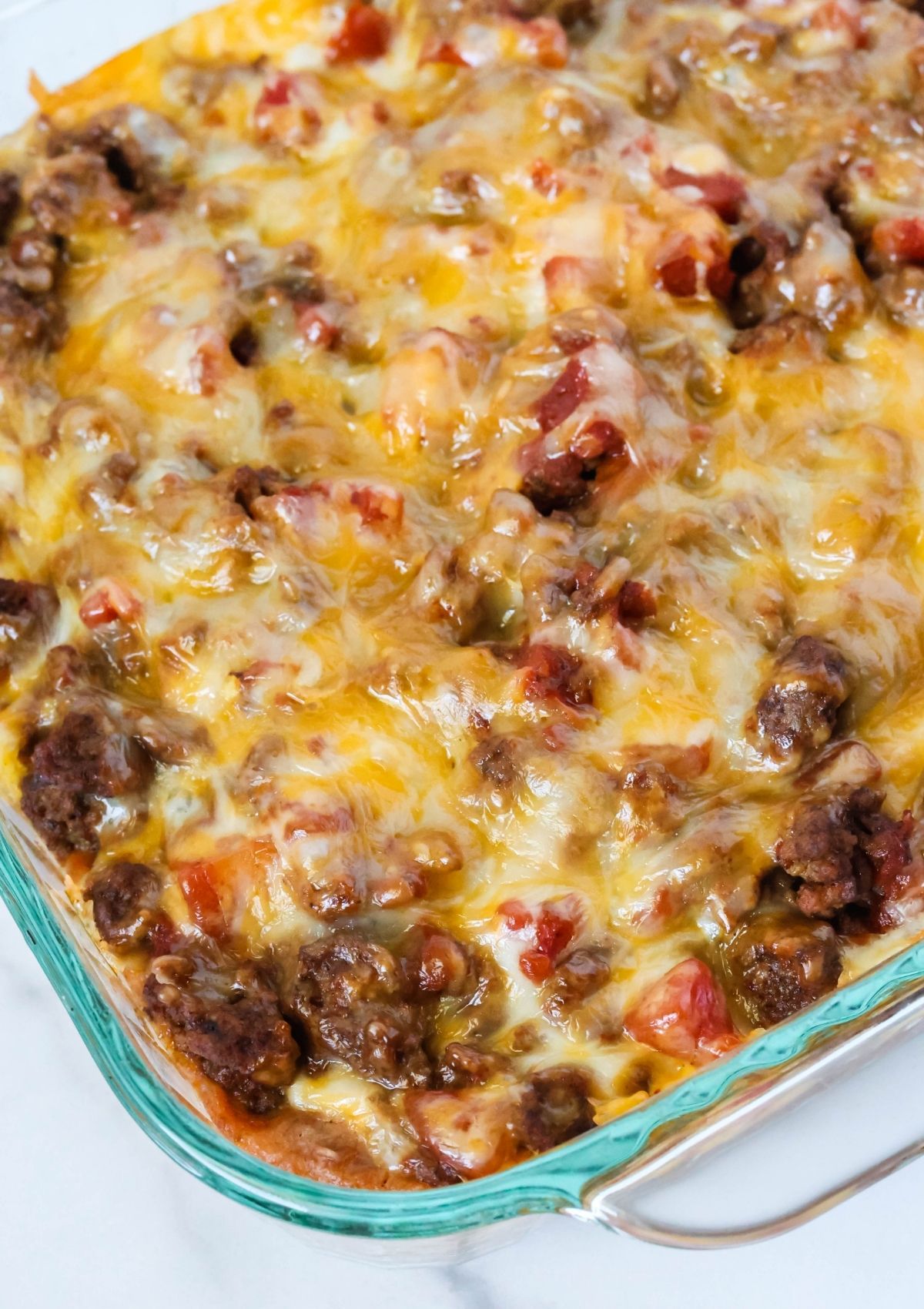 Close-up angled view of a baking dish filled with homemade taco casserole, showcasing the ground beef, melted cheese, and diced tomatoes.