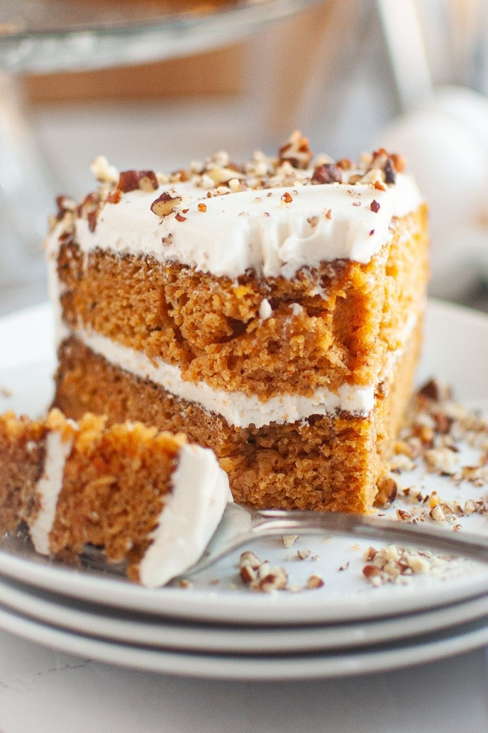 close-up view of a slice of carrot cake made with canned carrots, with a bite taken out of it. It's a two-layer cake with cream cheese frosting and chopped pecans on top.
