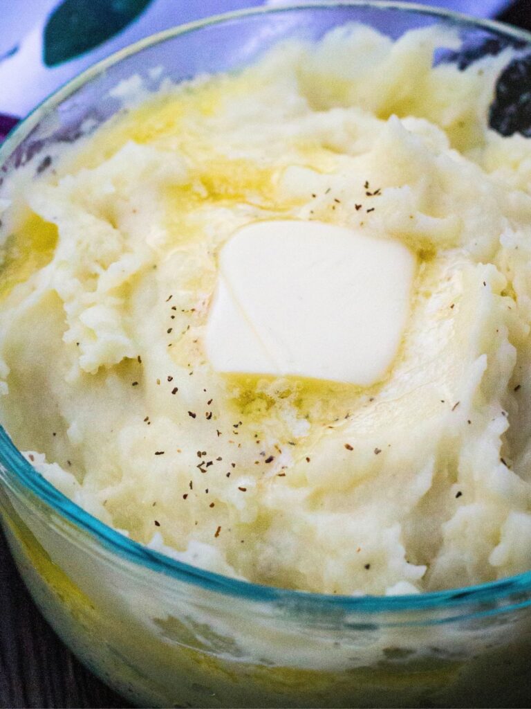 a glass dish of reheated mashed potatoes topped with a pat of butter and some salt and pepper.
