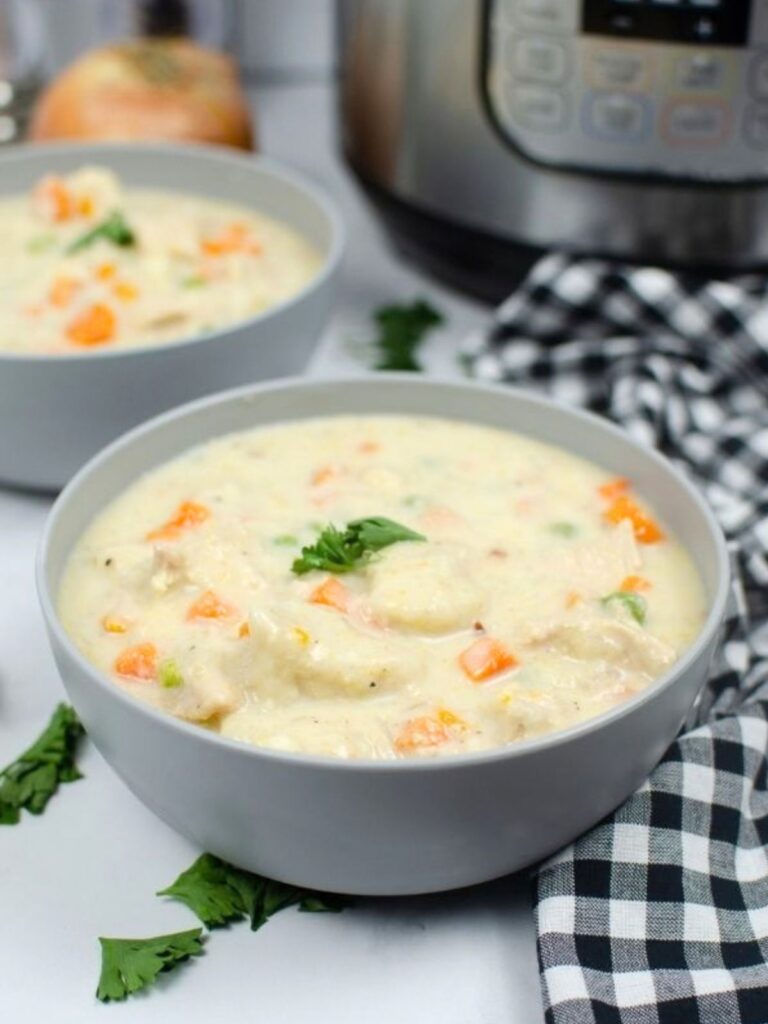 two bowls of Instant Pot chicken and dumplings made with biscuits, placed in front of an Instant Pot pressure cooker