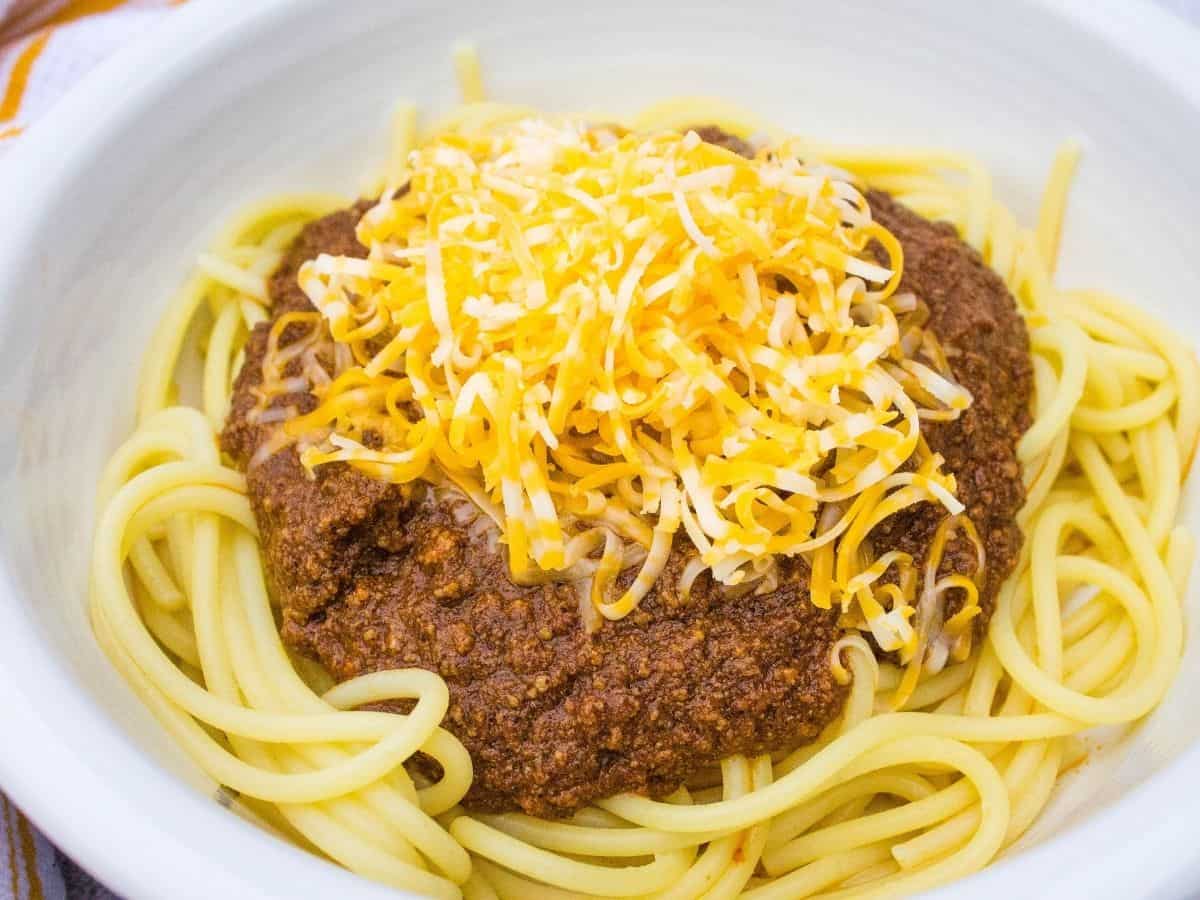 instant pot skyline chili topped with cheese and served over spaghetti in a white bowl