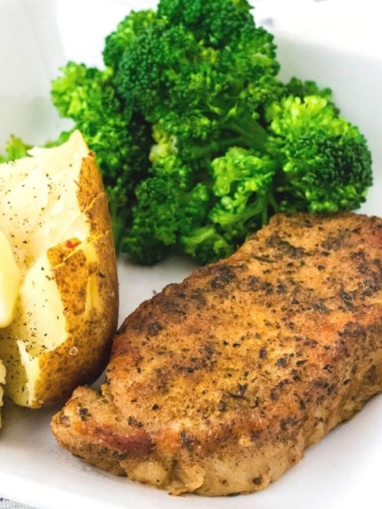Instant Pot pork chop on a white plate with broccoli and a baked potato.