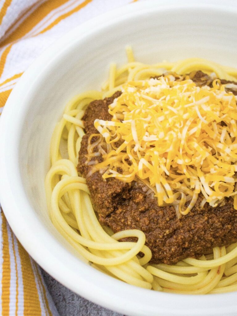 white bowl filled with spaghetti topped with Instant Pot Cincinnati Chili and shredded cheese
