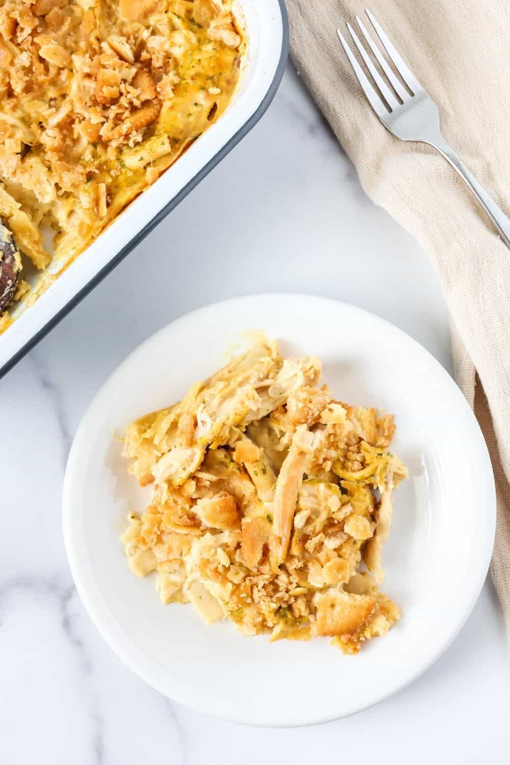 Overhead view of a serving of Knorr chicken and noodle casserole on a small white plate, with the baking dish of remaining casserole in the background.