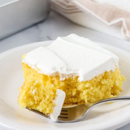 Slice of lemon pineapple cake on a white plate. A fork has cut a bite out of the slice.