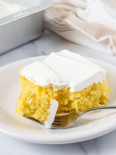 Slice of lemon pineapple cake on a white plate. A fork has cut a bite out of the slice.