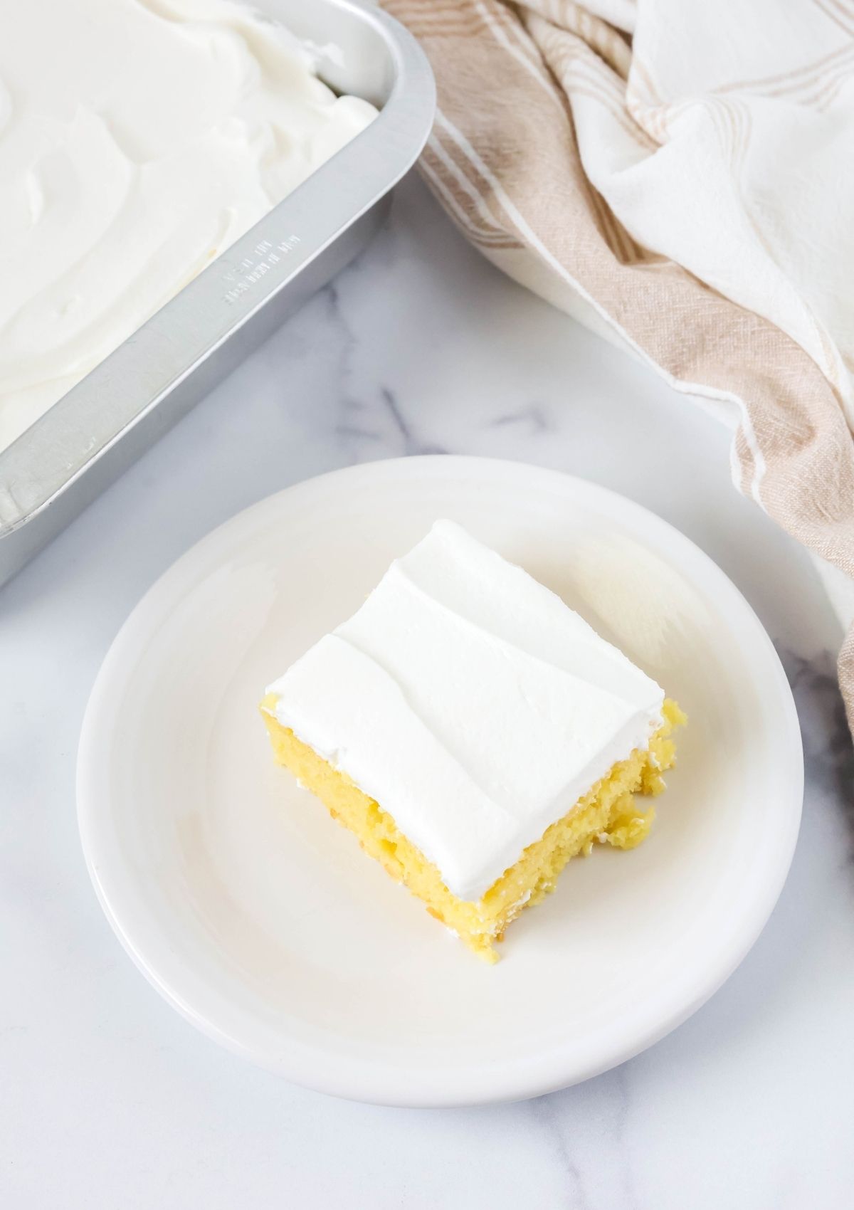 Overhead view of a slice of pineapple and lemon cake on a white plate, topped with Cool Whip.