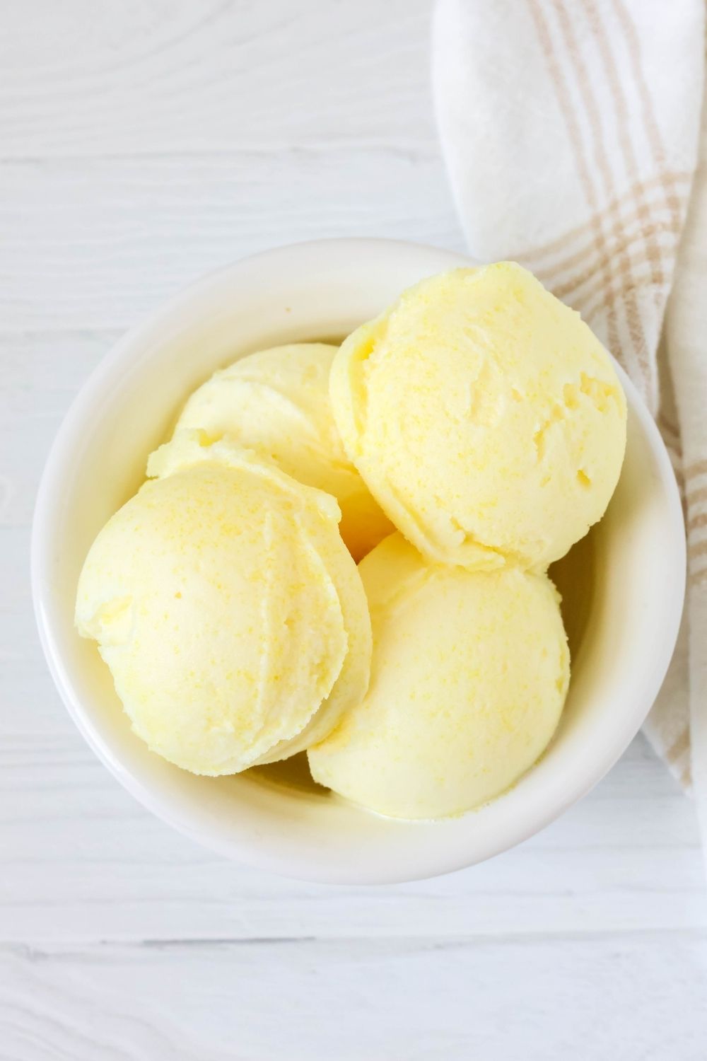 Overhead view of scoops of lemon sorbet made with Jell-O, served in a white dessert bowl.
