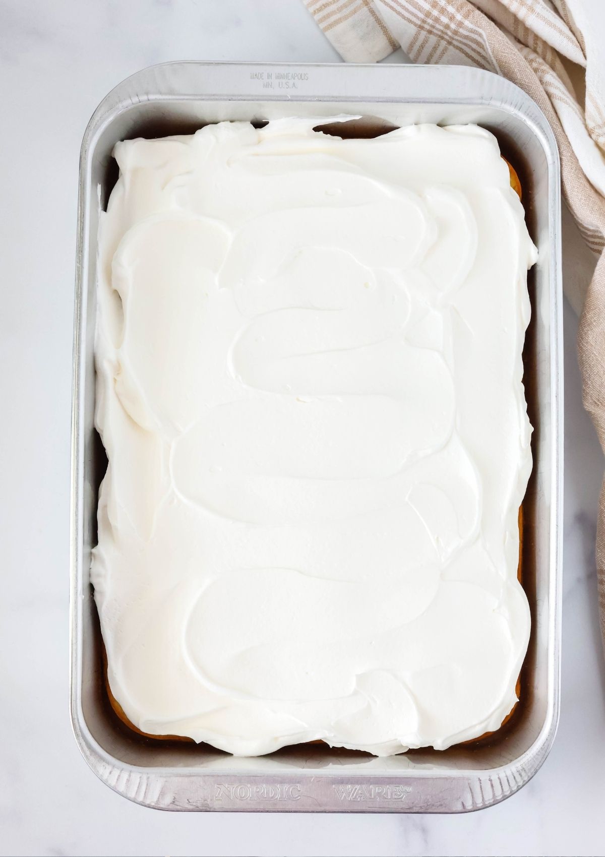 Overhead view of a 9x13-inch cake pan filled with lemon pineapple cake topped with whipped cream.