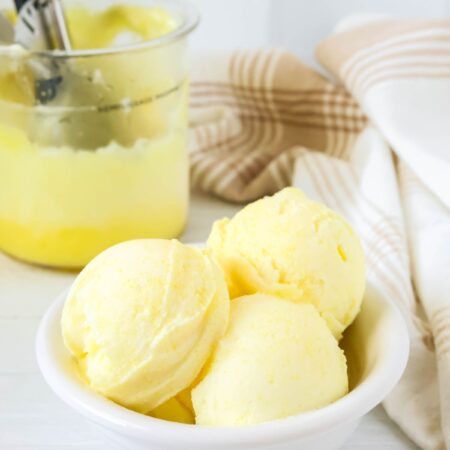 Scoops of Ninja Creami lemon sorbet served in a white bowl, with the Ninja Creami pint container of remaining sorbet in the background.