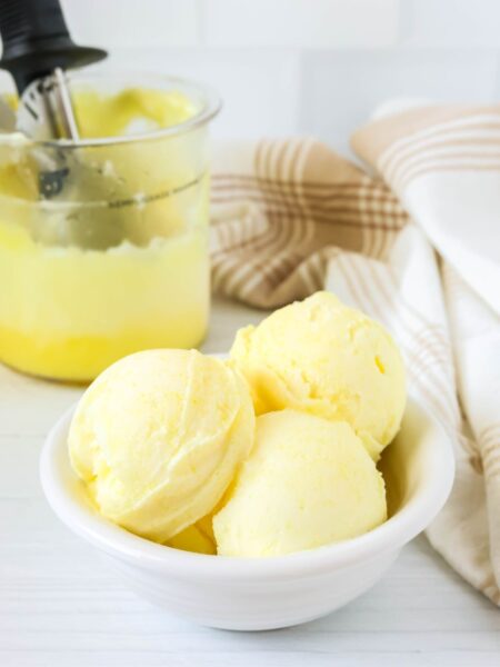 Scoops of Ninja Creami lemon sorbet served in a white bowl, with the Ninja Creami pint container of remaining sorbet in the background.