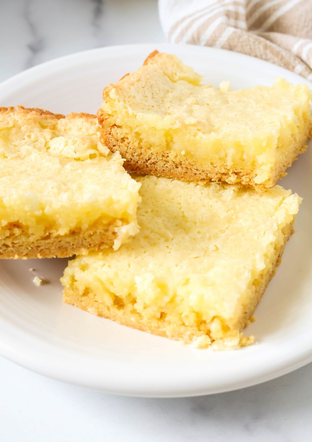 Close-up view of ooey gooey butter cake bars for a potluck dessert, served on a white plate.