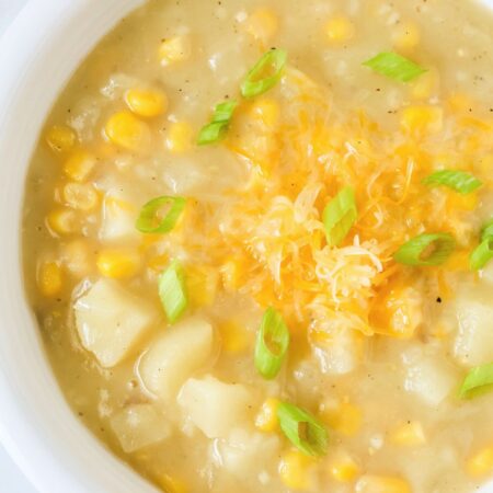 Potato corn chowder served in a white bowl, garnished with shredded cheese and sliced green onions.