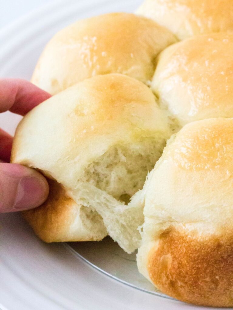 Fingers pull a dinner roll from a pan of previously frozen rolls that were risen in the Instant Pot.