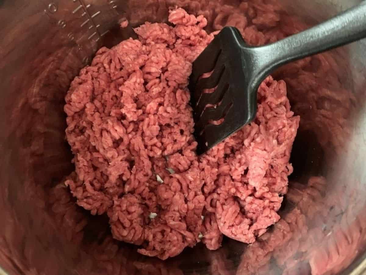 A spatula breaking apart ground beef in the insert pot of the Instant Pot.