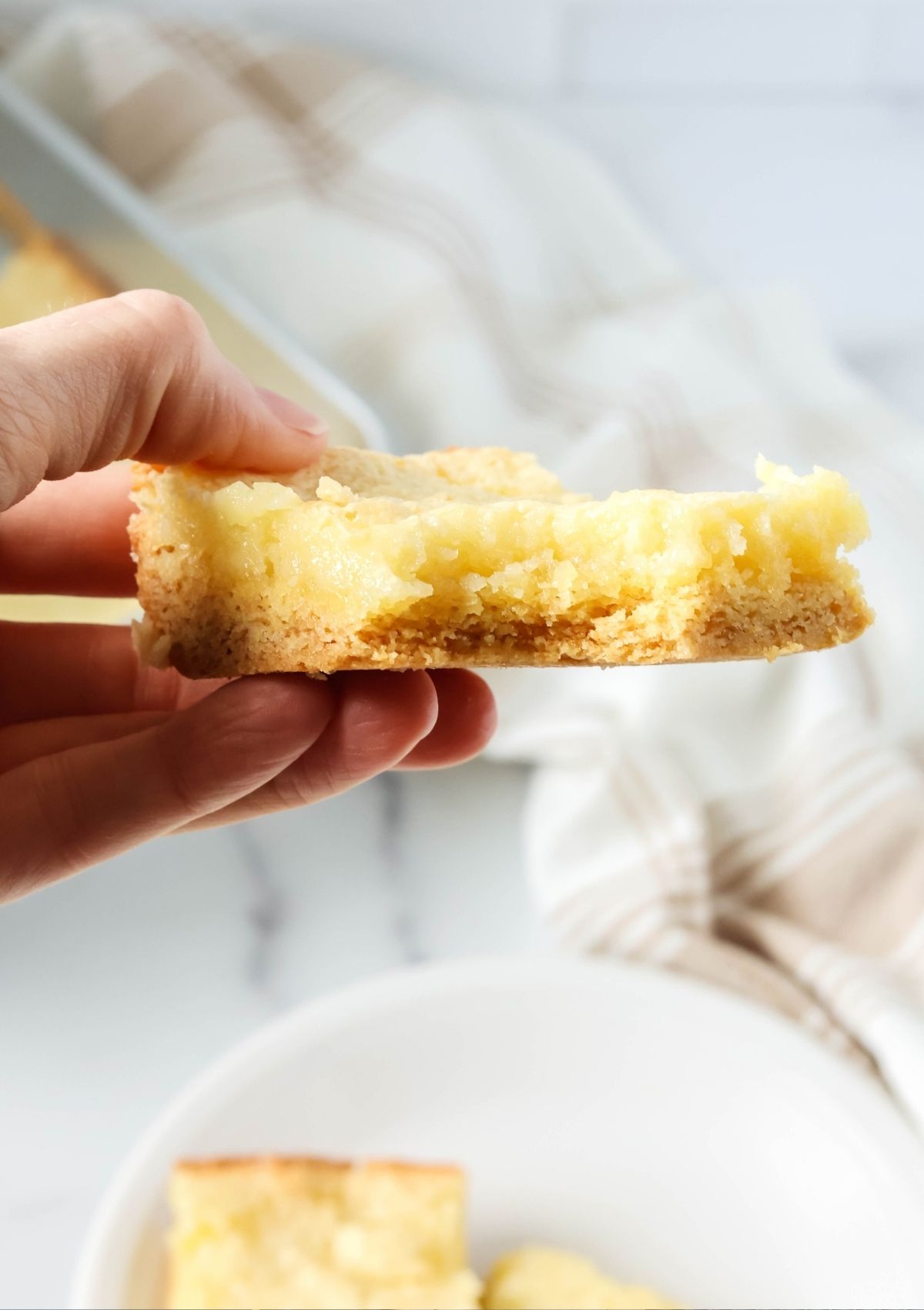 Close-up view of a hand holding an ooey gooey square with a bite taken out of it, showcasing the crust on the bottom and the soft filling on top.