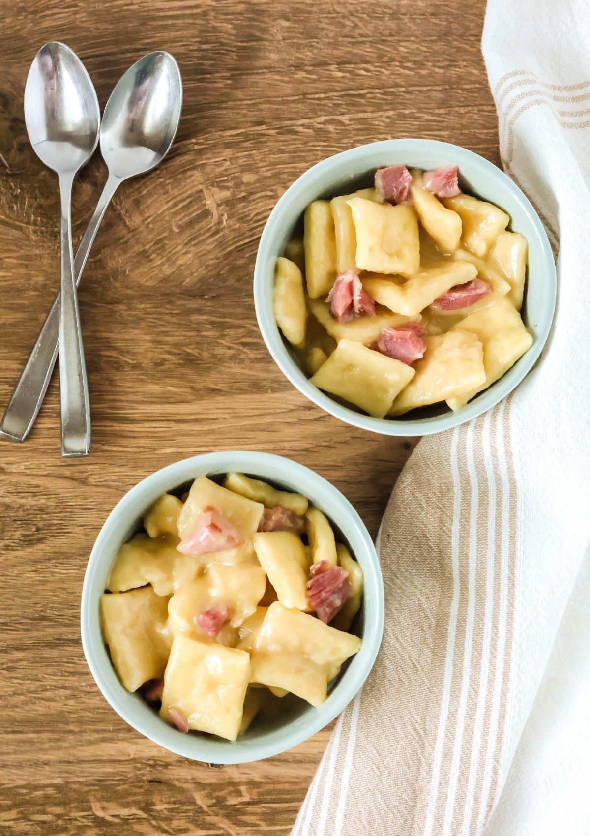 Two blue bowls filled with ham and dumplings. Two spoons are next to the bowl.