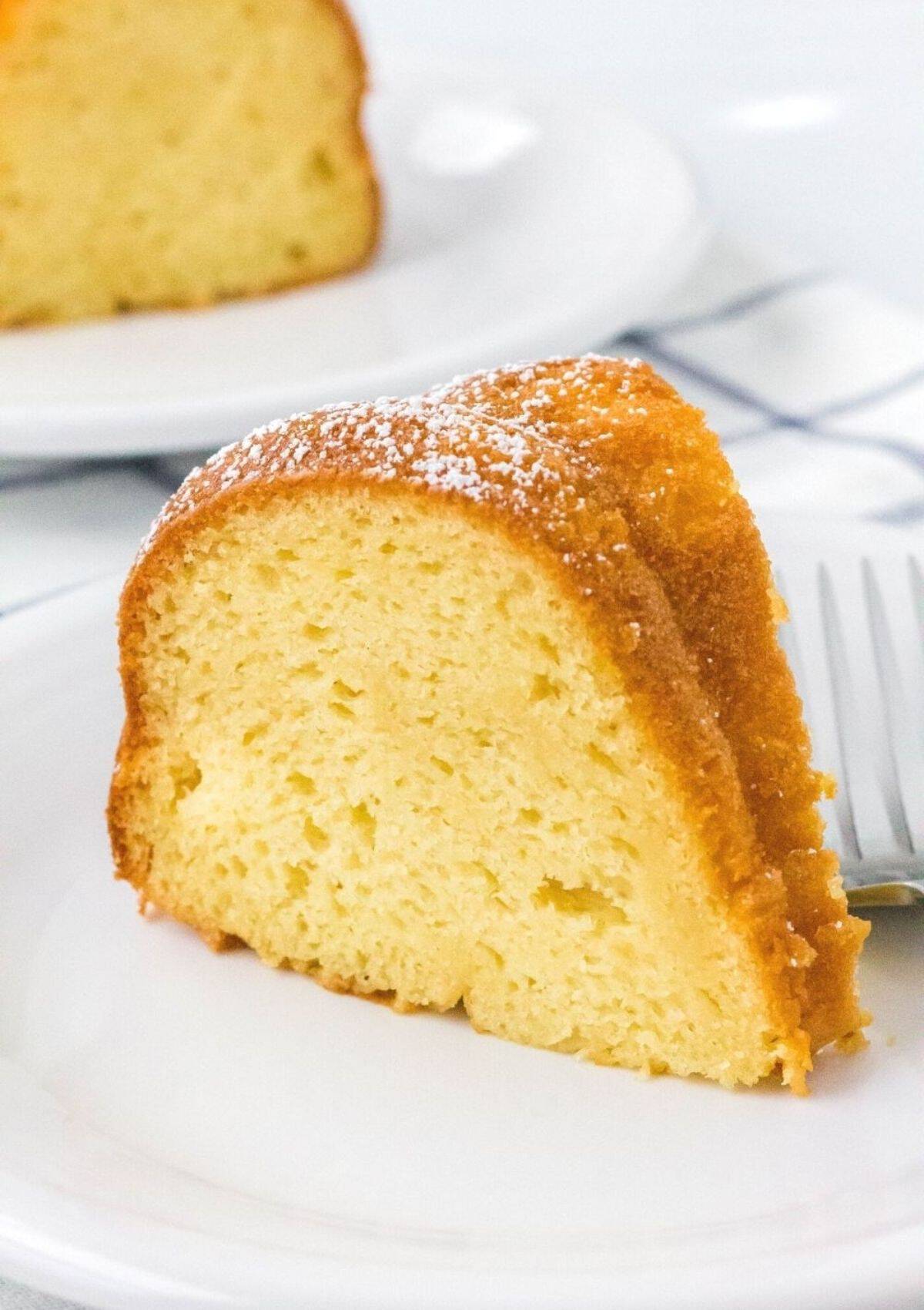 upright slice of vanilla pudding cake served on a white plate with a fork, demonstrating the moist interior of the cake