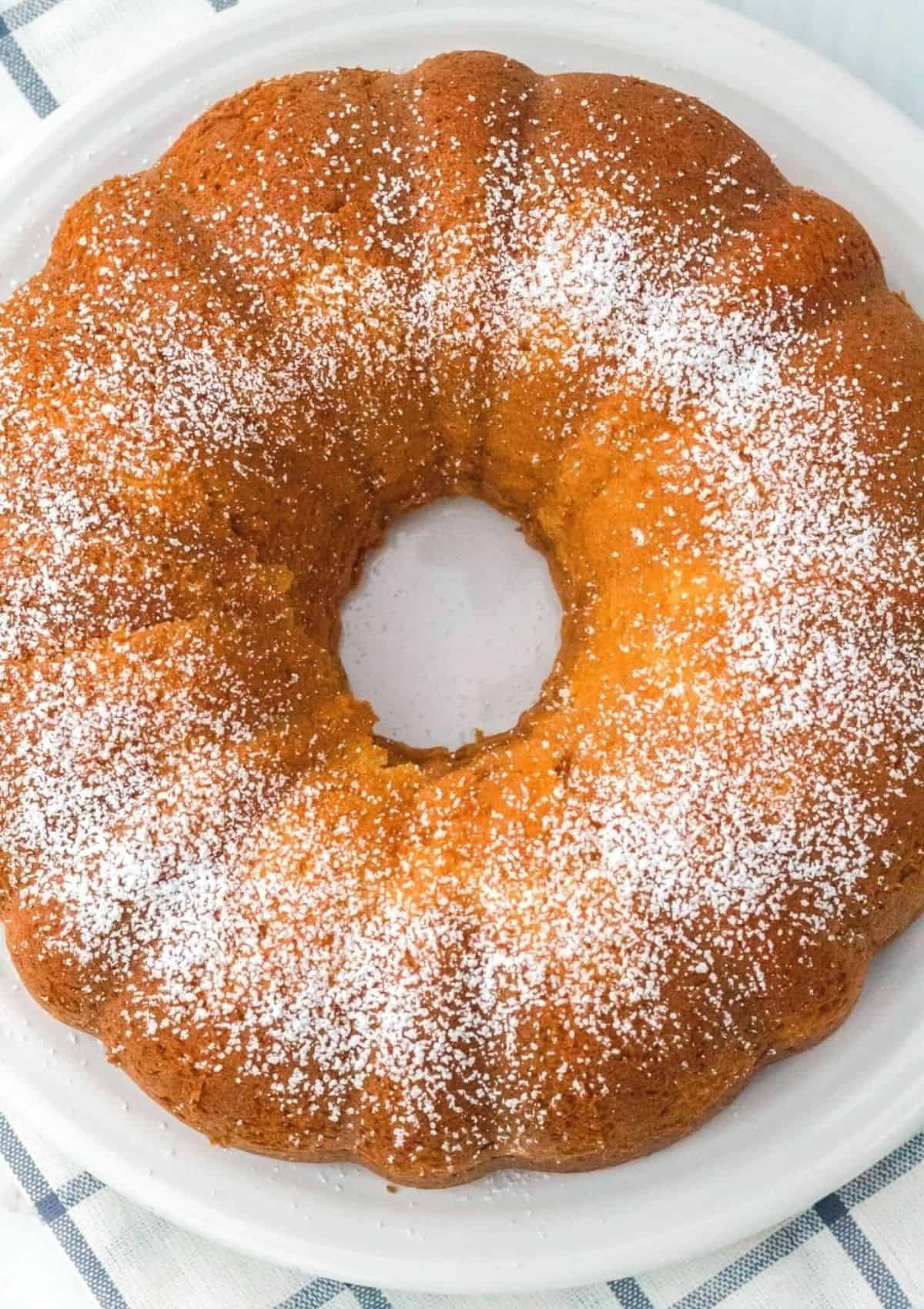 overhead view of vanilla pudding cake on a white plate, dusted with powdered sugar and ready to serve