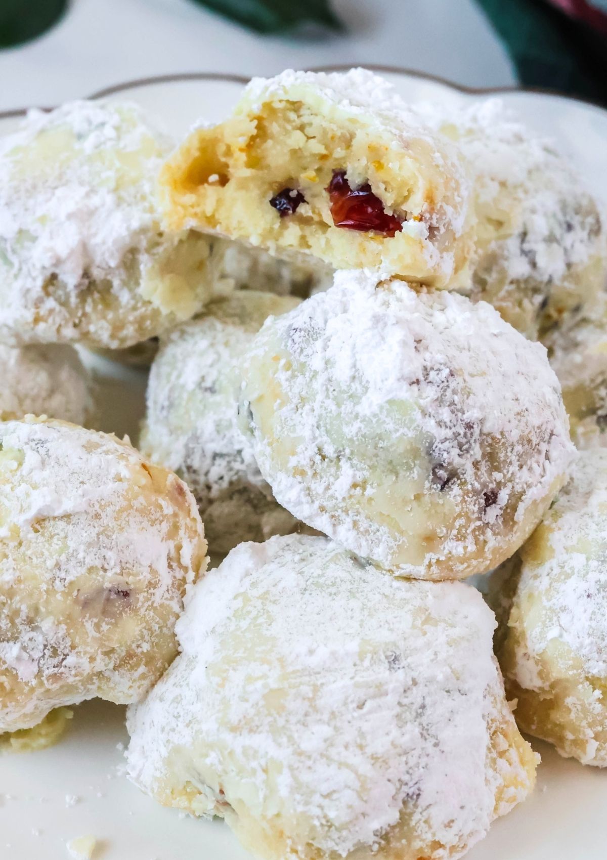 Close-up view of orange cranberry snowball cookies stacked together; one cookie has a bite taken out of it, showcasing the dried cranberries in the cookies.