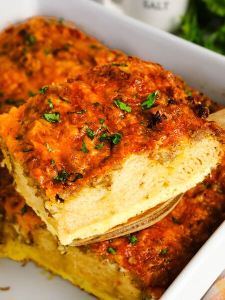 A spatula lifts a slice of biscuit breakfast bake from the baking dish, showcasing the layers of biscuit, eggs, sausage, and cheese in the casserole.