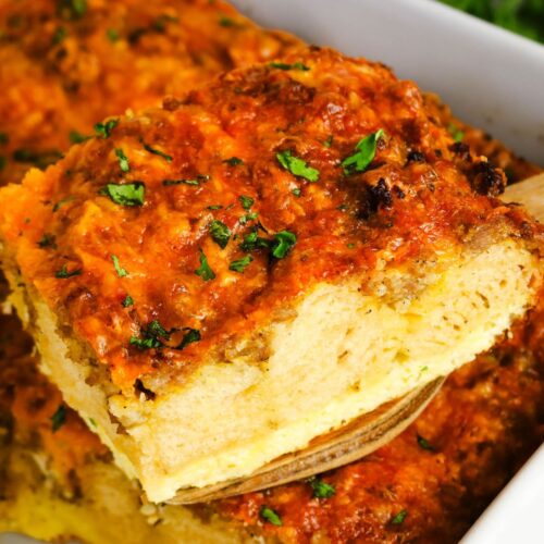 A spatula lifts a slice of biscuit breakfast bake from the baking dish, showcasing the layers of biscuit, eggs, sausage, and cheese in the casserole.