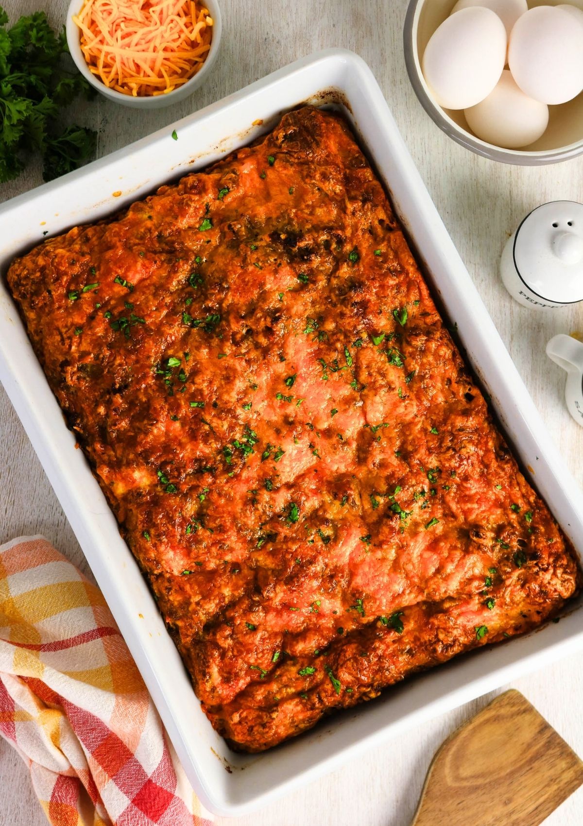 Overhead view of a white baking dish of cheesy sausage egg breakfast casserole made with canned biscuits.