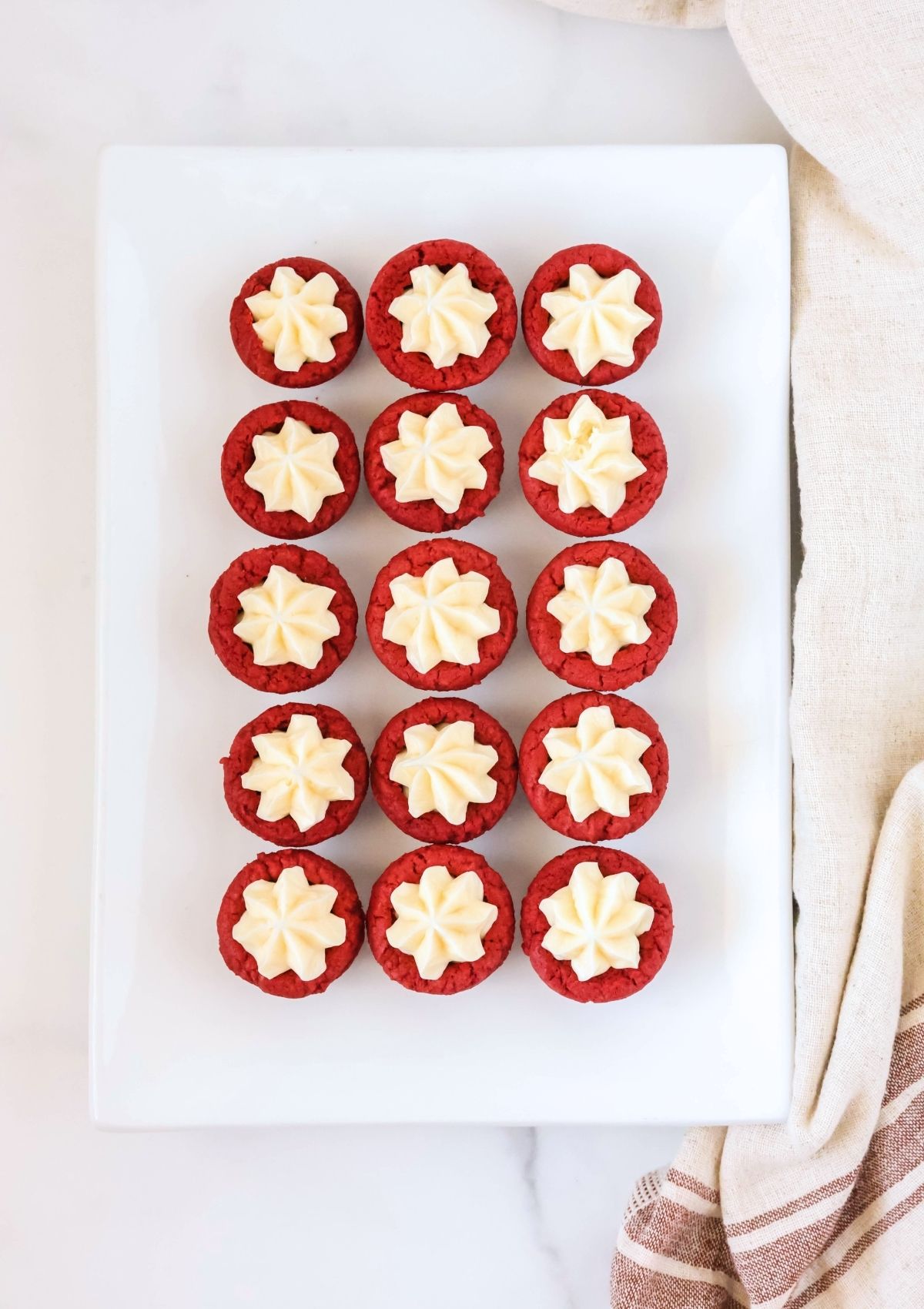 Overhead view of several cake mix red velvet cookie cups with frosting, served on a rectangular platter.