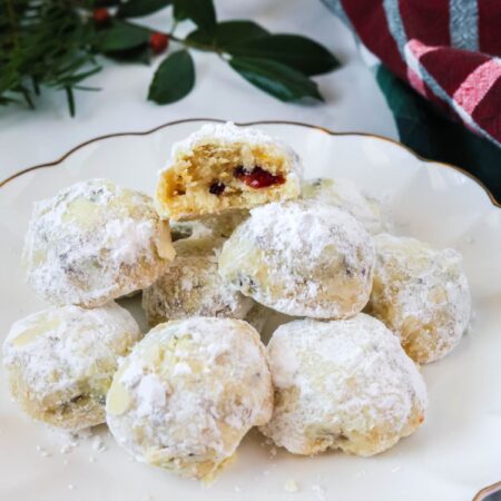 Cranberry orange snowball cookies served on a white plate. Festive greenery and a plaid kitchen towel are in the background.