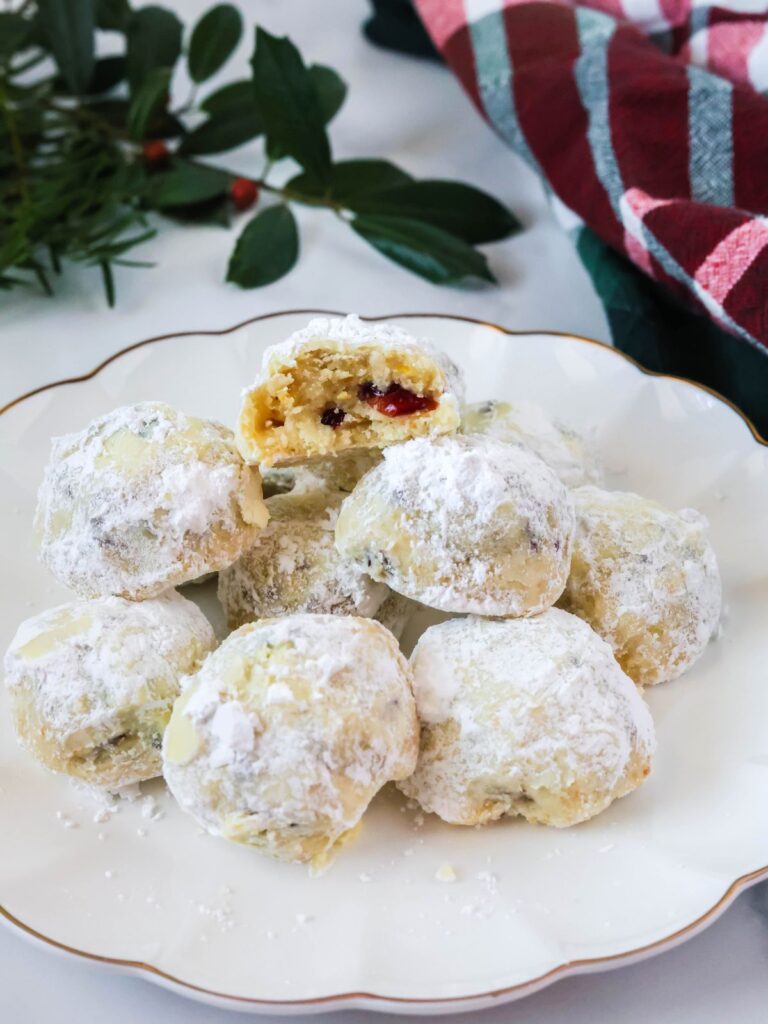 Cranberry orange snowball cookies served on a white plate. Festive greenery and a plaid kitchen towel are in the background.