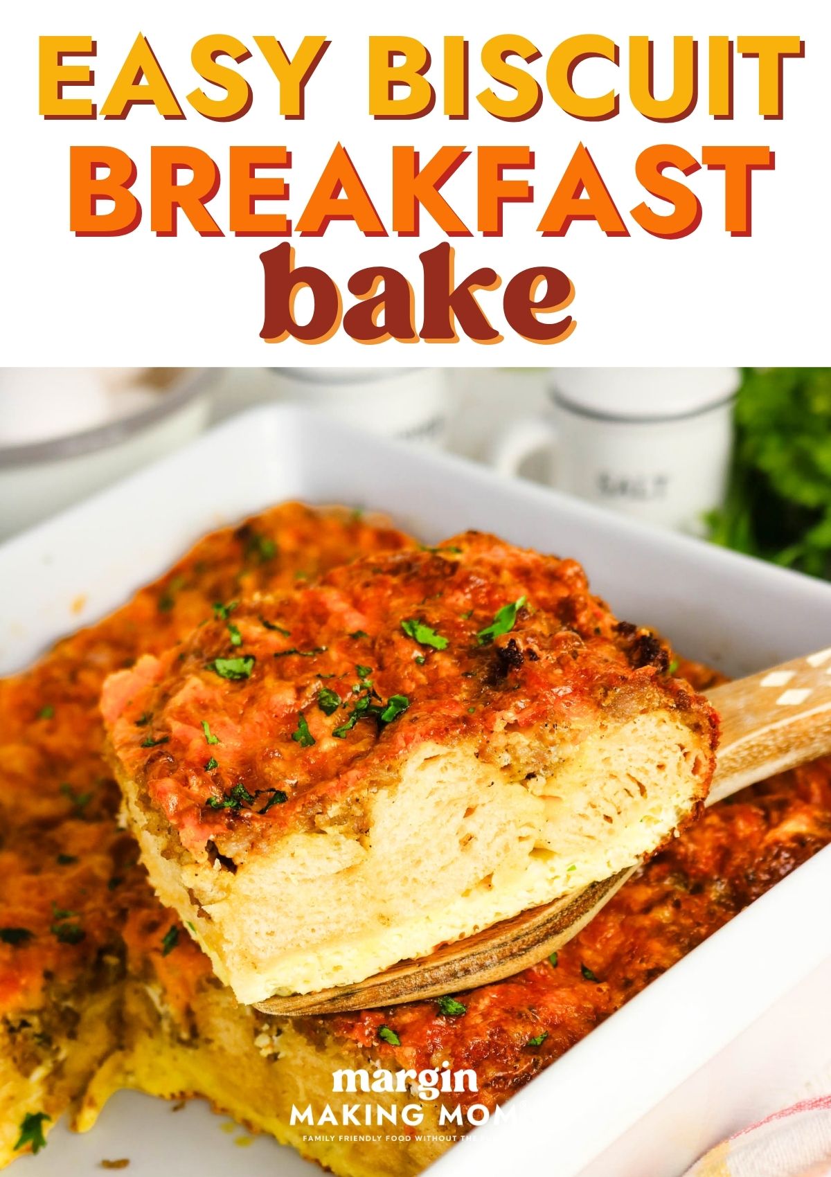A wooden spatula lifts a slice of easy biscuit breakfast bake from a baking dish, showcasing the layers of biscuit, egg, sausage, and cheese.