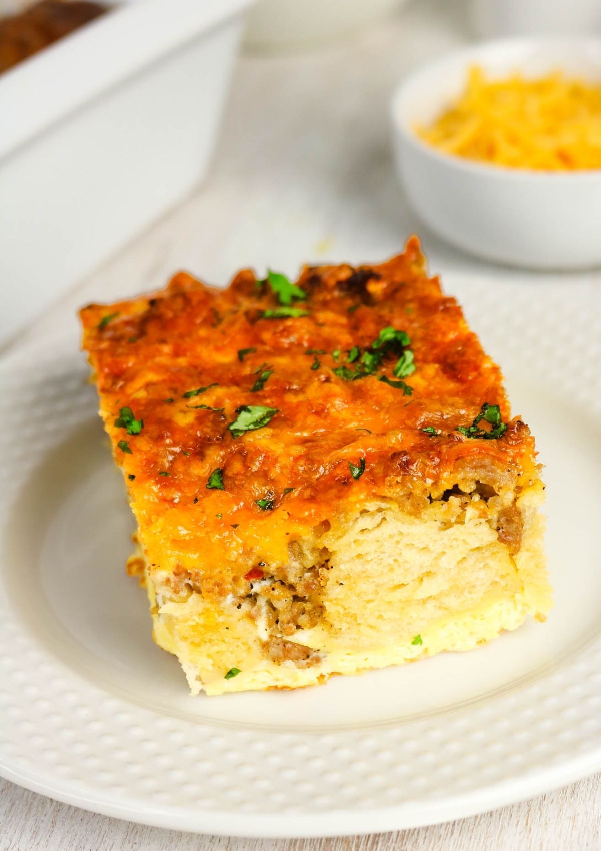 Slice of breakfast casserole made with Pillsbury Grands biscuits, served on a white plate, showcasing the sausage, egg, and cheese baked into the biscuit pieces.
