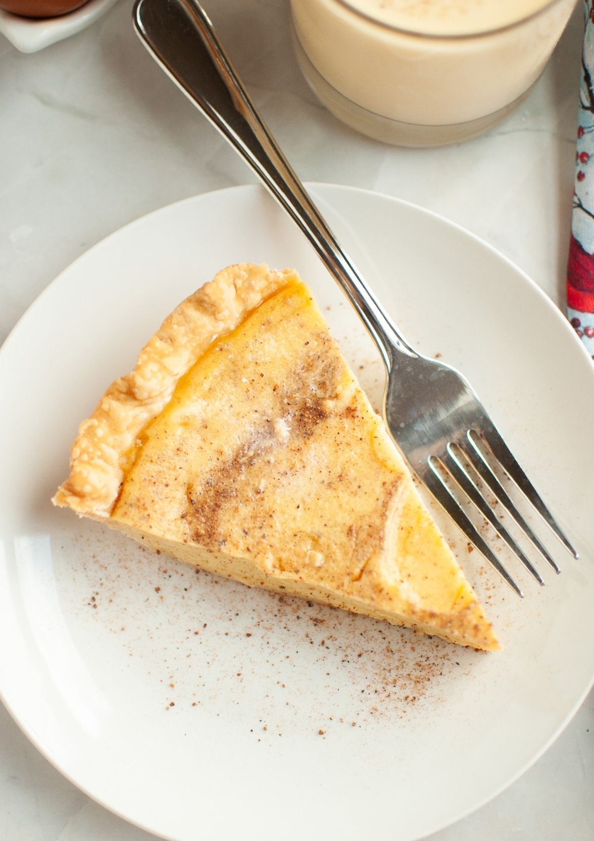 Overhead view of a slice of eggnog custard pie on a white plate with a fork.