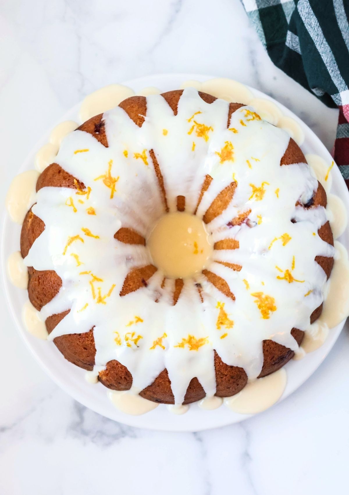 Overhead view of a cranberry orange bundt cake on a white serving plate, topped with icing and grated orange zest.