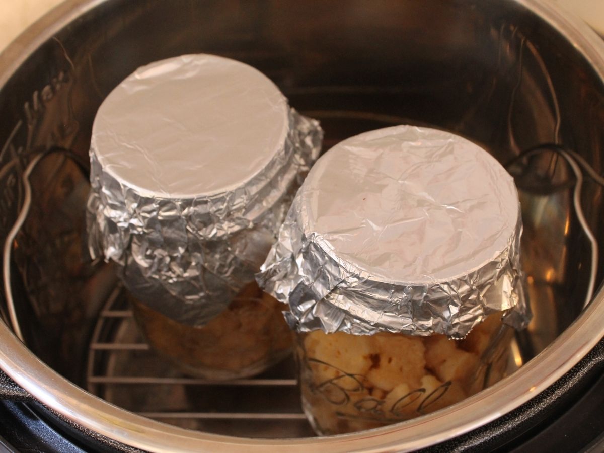 Two glass jars of leftovers, covered with aluminum foil, on the trivet in the Instant Pot for reheating the food.