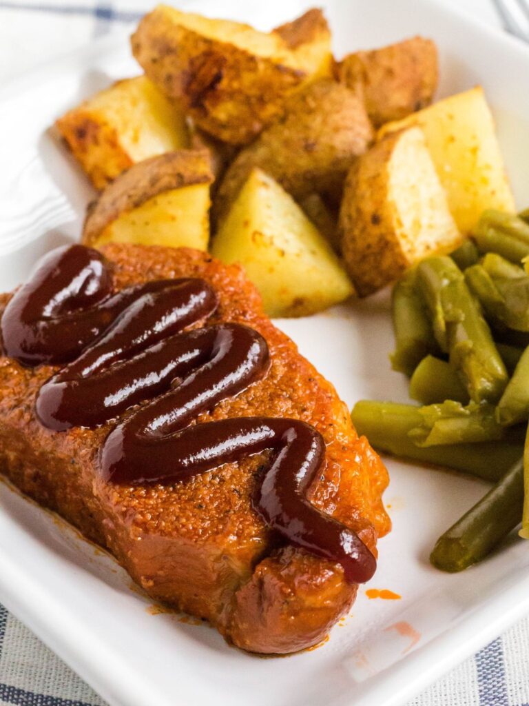 Instant Pot BBQ pork chop, topped with a swirl of BBQ sauce, served on a white plate with green beans and roasted potatoes.