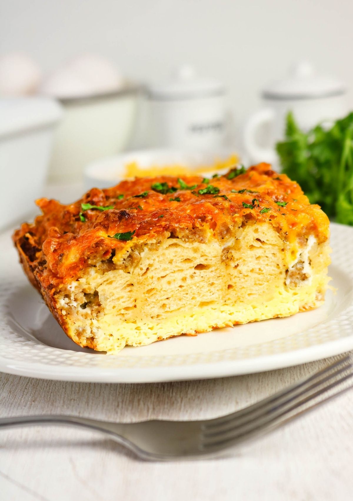 Side view of a slice of make-ahead sausage, egg, and cheese breakfast casserole made with canned biscuits, served on a white plate.