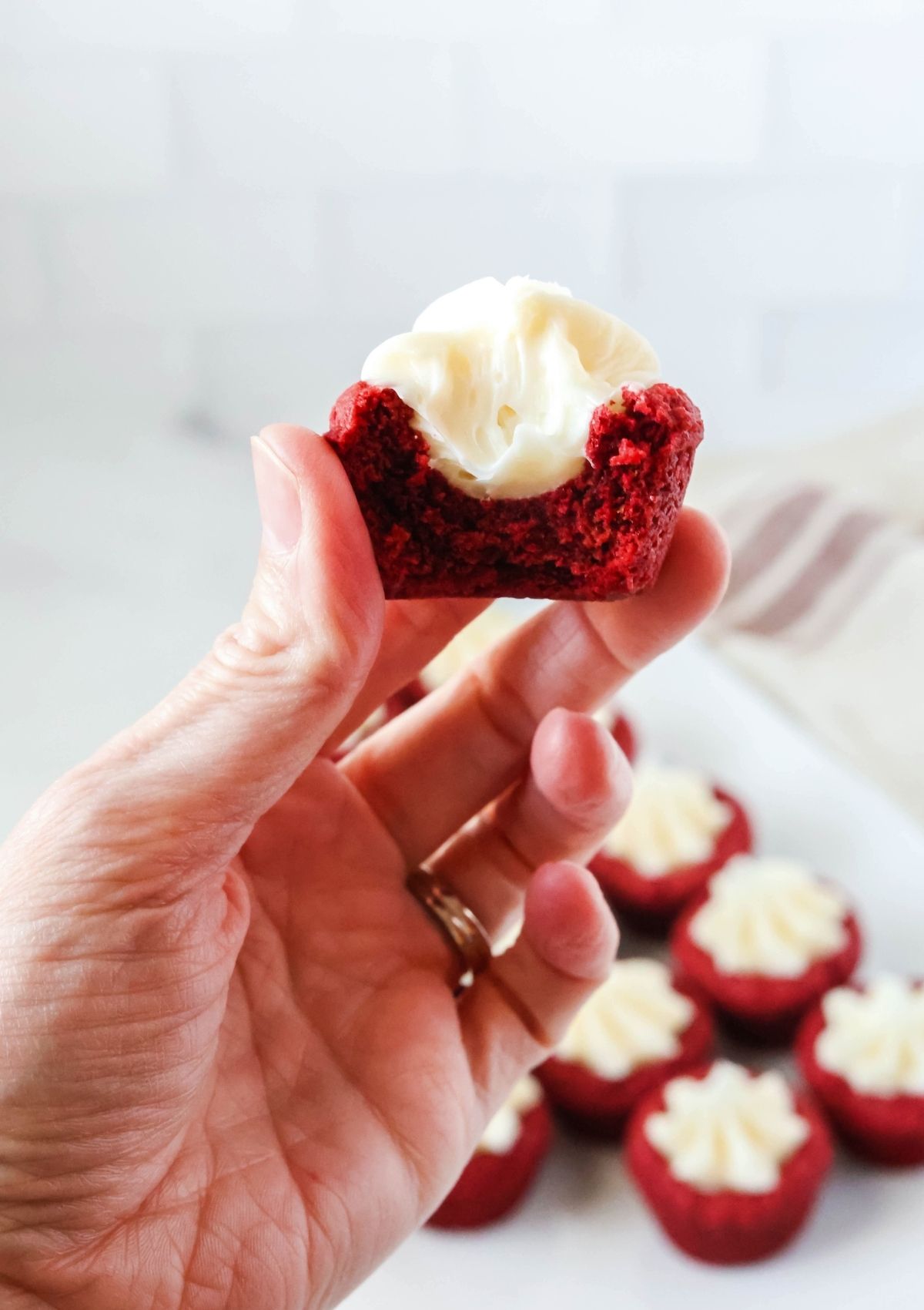 A woman's hand holds a red velvet cookie cup with a bite taken out of it.