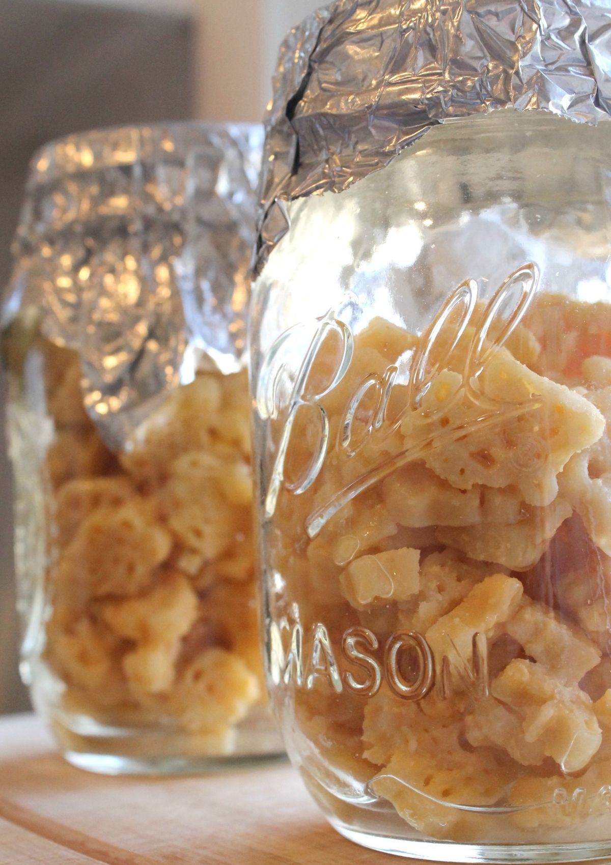Side view of two jars containing leftover macaroni and cheese. The jars are covered with aluminum foil for reheating the pasta in the Instant Pot.