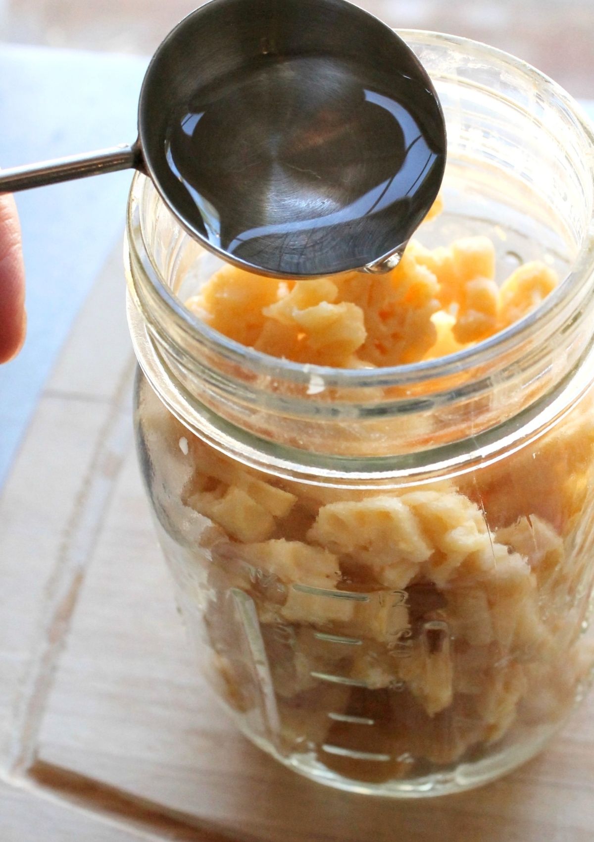 A measuring spoon is used to add a small amount of water to a jar of leftovers for reheating in the Instant Pot.